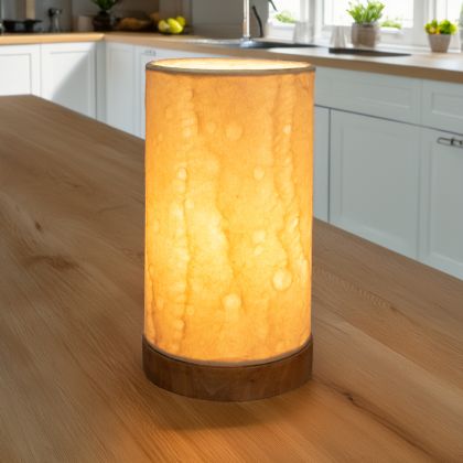 In a sun drenched entryway, crafted by the artisans of Eangee Home Design, the Mini Paper Cylinder Table Lamp Wave in natural stands gracefully, featuring reclaimed mango wood base, recycled paper shade, sustainably sourced, recycled materials, adding warmth and character to the space.