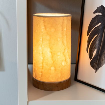 In a minimalist loft with natural textures, crafted by the artisans of Eangee Home Design, the Mini Paper Cylinder Table Lamp Wave in natural stands gracefully, featuring reclaimed mango wood base, recycled paper shade, sustainably sourced, recycled materials, adding warmth and character to the space.