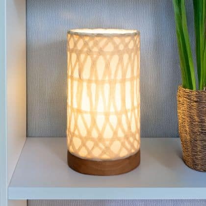 In a quiet bedside corner, crafted by the artisans of Eangee Home Design, the Mini Paper Cylinder Table Lamp Arches in natural stands gracefully, featuring reclaimed mango wood base, recycled paper shade, sustainably sourced, recycled materials, adding warmth and character to the space.
