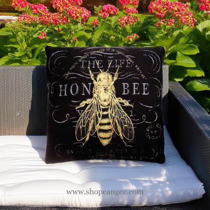 In a shaded porch swing a multi colored outdoor pillow crafted by the artisans of Magnolia Casual called the Outdoor Pillow Vintage Bee 18x18 is displayed featuring 100 percent weather resistant fabric, weather resistant polyester fabric adding comfort and style to the space featuring with a bee motif.