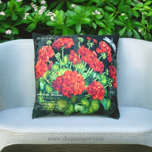 In an outdoor reading nook a red outdoor pillow crafted by the artisans of Magnolia Casual called the Outdoor Pillow Red Geranium is displayed featuring handwoven textile adding comfort and style to the space featuring shades of red.