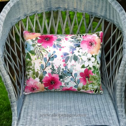 In an outdoor reading nook a multi colored outdoor pillow crafted by the artisans of Magnolia Casual called the Outdoor Pillow Meadow Dance 1 19x24 is displayed featuring 100 percent weather resistant fabric adding comfort and style to the space.