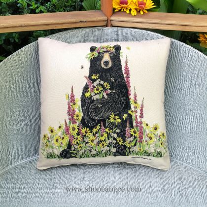 In a shaded porch swing a multi colored outdoor pillow crafted by the artisans of Magnolia Casual called the Outdoor Pillow Wildflower & Bear 18x18 is displayed featuring handwoven textile adding comfort and style to the space.