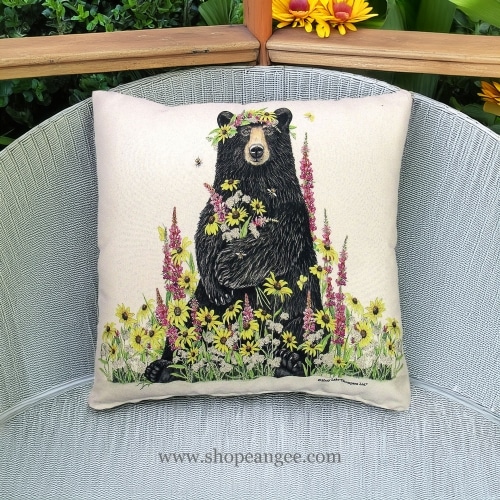 In a shaded porch swing a multi colored outdoor pillow crafted by the artisans of Magnolia Casual called the Outdoor Pillow Wildflower & Bear 18x18 is displayed featuring handwoven textile adding comfort and style to the space.