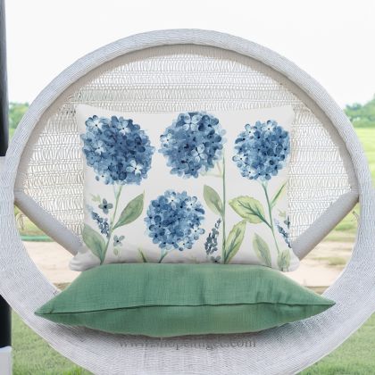 In a cozy garden seating area a multi colored outdoor pillow crafted by the artisans of Magnolia Casual called the Outdoor Pillow Four Hydrangeas 19x24 is displayed featuring handwoven textile, natural materials adding comfort and style to the space.
