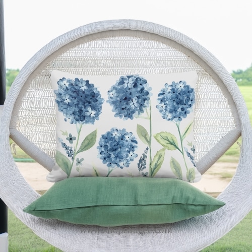 In a cozy garden seating area a multi colored outdoor pillow crafted by the artisans of Magnolia Casual called the Outdoor Pillow Four Hydrangeas 19x24 is displayed featuring handwoven textile, natural materials adding comfort and style to the space.