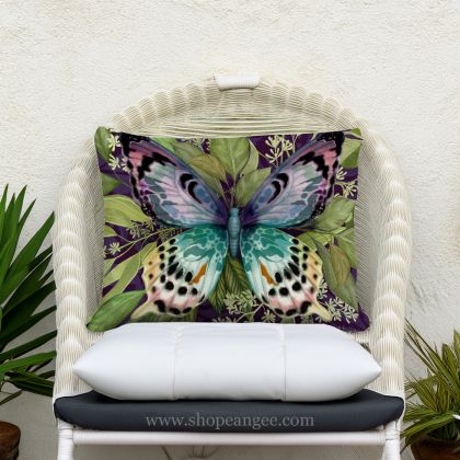 In a shaded porch swing a multi colored outdoor pillow crafted by the artisans of Magnolia Casual called the Outdoor Pillow Mystic Butterfly 19x24 is displayed featuring quality outdoor fabric adding comfort and style to the space featuring with a butterfly motif.