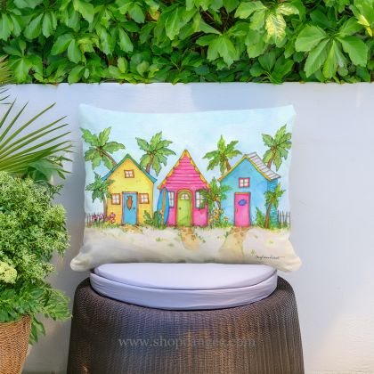 In a sunlit patio lounge a multi colored outdoor pillow crafted by the artisans of Magnolia Casual called the Outdoor Pillow Colorful Beach Cottages 19x24 is displayed featuring quality outdoor fabric, eco friendly adding comfort and style to the space.