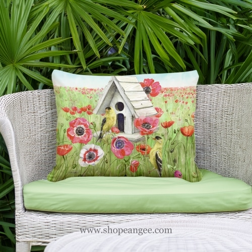 In a cozy garden seating area a yellow outdoor pillow crafted by the artisans of Magnolia Casual called the Outdoor Pillow Yellow Birds and Poppy Field 19x24 is displayed featuring handwoven textile adding comfort and style to the space featuring shades of yellow.