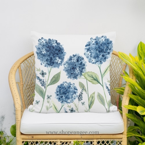 In a poolside chaise a multi colored outdoor pillow crafted by the artisans of Magnolia Casual called the Outdoor Pillow Four Hydrangeas 18x18 is displayed featuring handwoven textile, natural materials adding comfort and style to the space.
