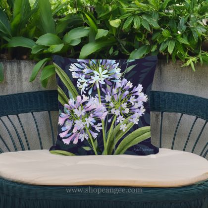 In a sunlit patio lounge a multi colored outdoor pillow crafted by the artisans of Magnolia Casual called the Outdoor Pillow Midnight Garden Lilies 18x18 is displayed featuring handwoven textile adding comfort and style to the space.