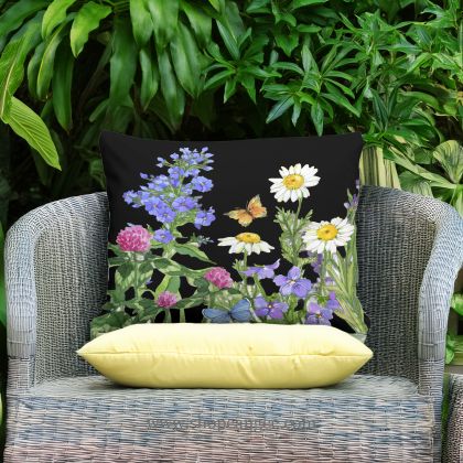 In an outdoor reading nook a multi colored outdoor pillow crafted by the artisans of Magnolia Casual called the Outdoor Pillow Garden Meadow 2 13x18 is displayed featuring handwoven textile adding comfort and style to the space.