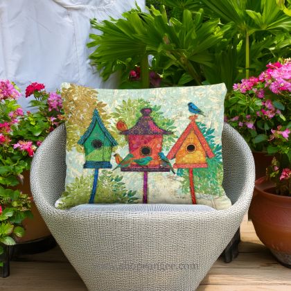 In an outdoor reading nook a multi colored outdoor pillow crafted by the artisans of Magnolia Casual called the Outdoor Pillow 3 Birdhouses 13x18 is displayed featuring quality outdoor fabric adding comfort and style to the space.