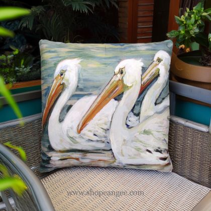 In a shaded porch swing a multi colored outdoor pillow crafted by the artisans of Magnolia Casual called the Outdoor Pillow 3 Pelicans Swimming 18x18 is displayed featuring quality outdoor fabric adding comfort and style to the space.