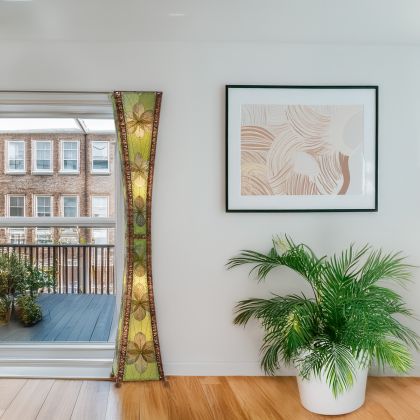 Green Hourglass Giant Floor Lamp by Eangee Home Design - sculptural hourglass tower clad in overlapping green cocoa leaf panels and abaca accents; artisan-made piece casts soothing organic light beside modern artwork.