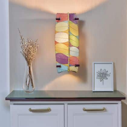 Eangee Home Design Banana Wall Sconce in multicolor with a shade made of real cocoa leaves, brightening a hallway vignette with glass?topped cabinet and botanical art