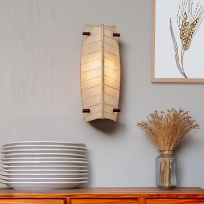 Eangee Home Design Banana Wall Sconce in natural beige with a shade made of real cocoa leaves, adding warm ambient glow above a wooden sideboard and decorative plate