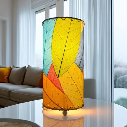 12 Inch Cocoa Leaf Cylinder Table Lamp Multi Color shade, handcrafted from real cocoa leaves . soft ambient light on a styled bookshelf with neutral ceramics and books.