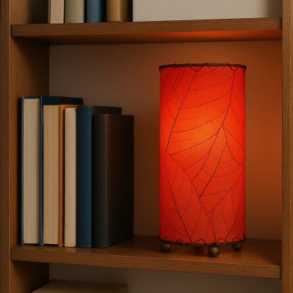 Handmade red leaf-patterned cylinder lamp by Eangee, placed on a wooden bookshelf surrounded by books.