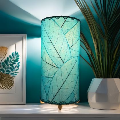 Sea blue Eangee mini cylinder lamp made with real fossilized cocoa leaves, glowing on a modern console with plant decor.